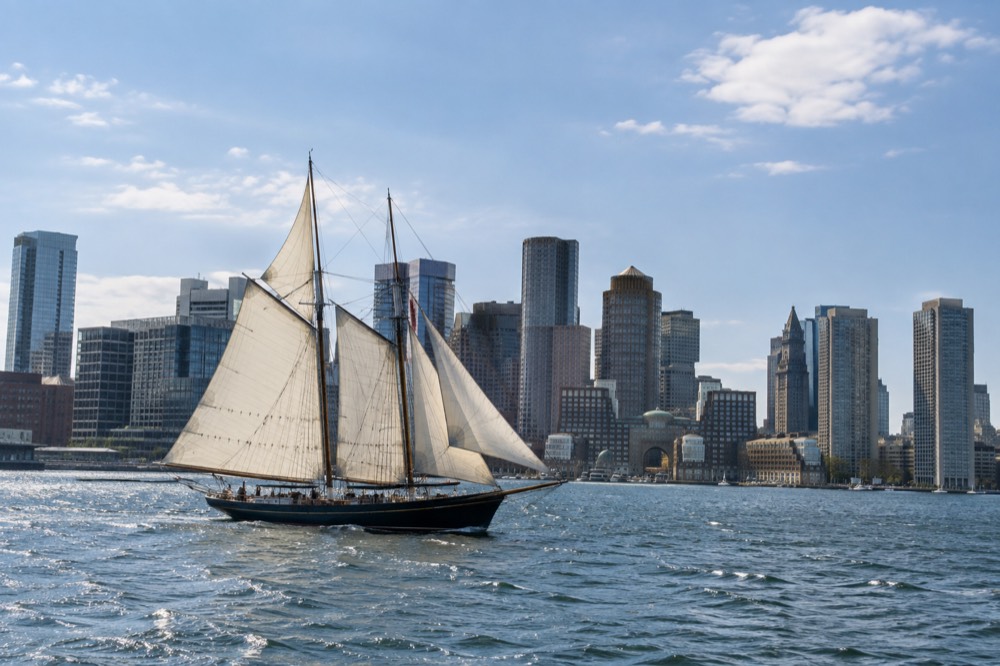 A tall ship under sail in Boston harbor with downtown buildings behind