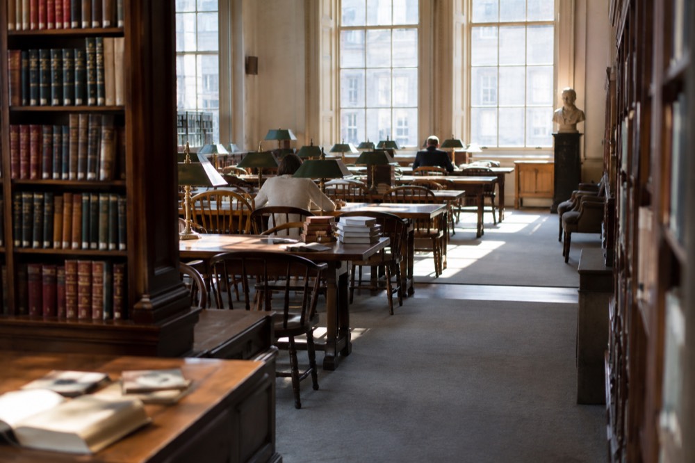 A quiet reading room inside the Boston Athenaeum with long tables, lamps, and shelves of books