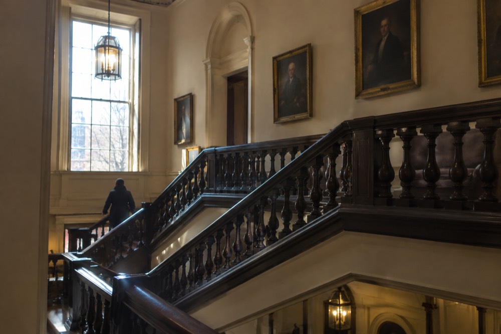 The grand central staircase inside the Boston Athenaeum with dark wood railings and portraits on the walls