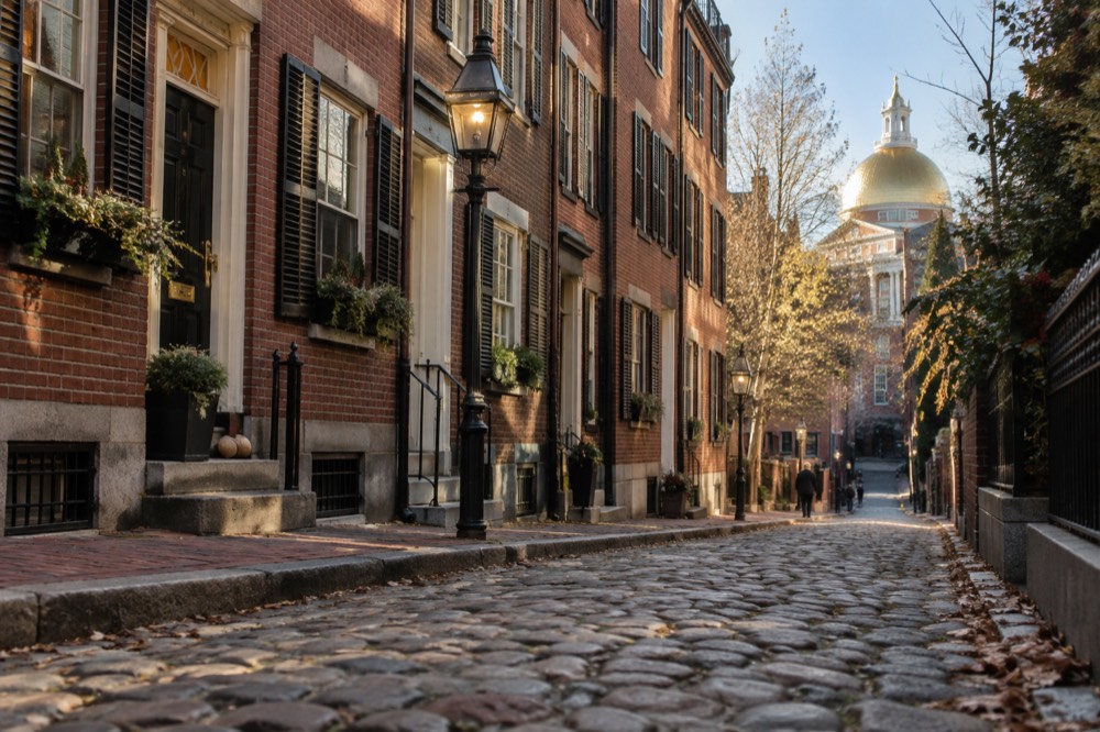 A brick rowhouse street on Beacon Hill with the gold dome of the State House visible nearby