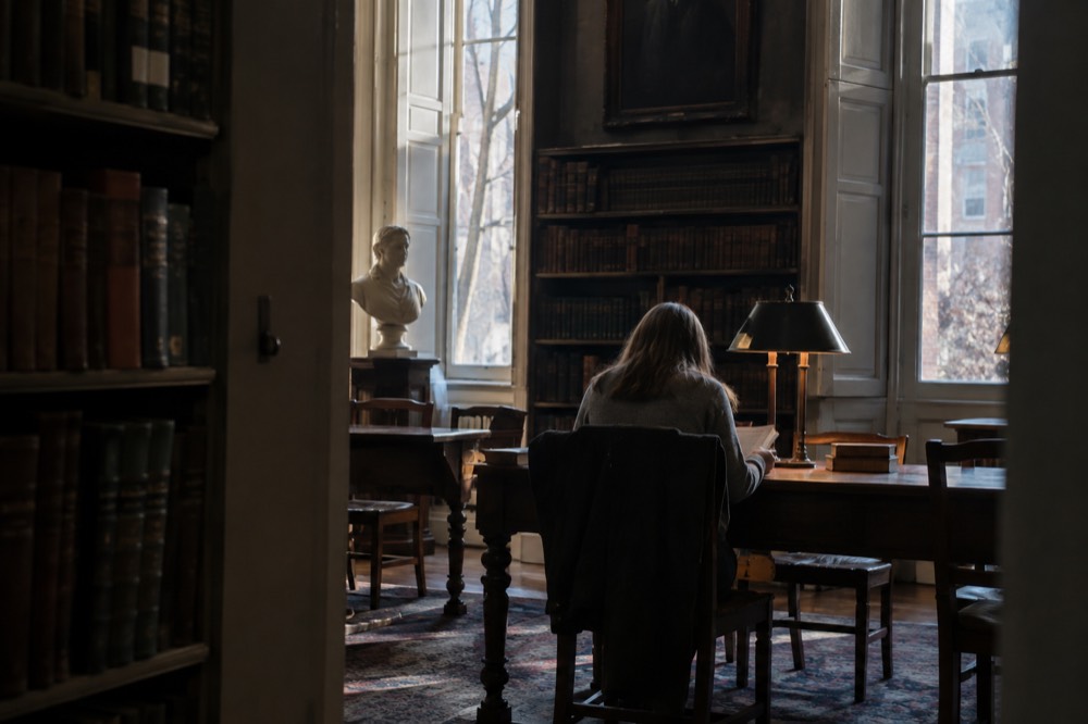 A visitor reading a book at a wooden table in a quiet corner of the Boston Athenaeum