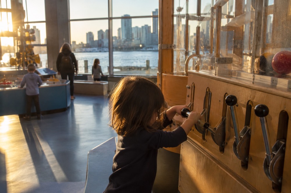 A child pressing levers on a wooden interactive machine exhibit in a museum gallery