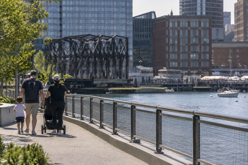 A family walking with a stroller along a waterfront path beside a city channel