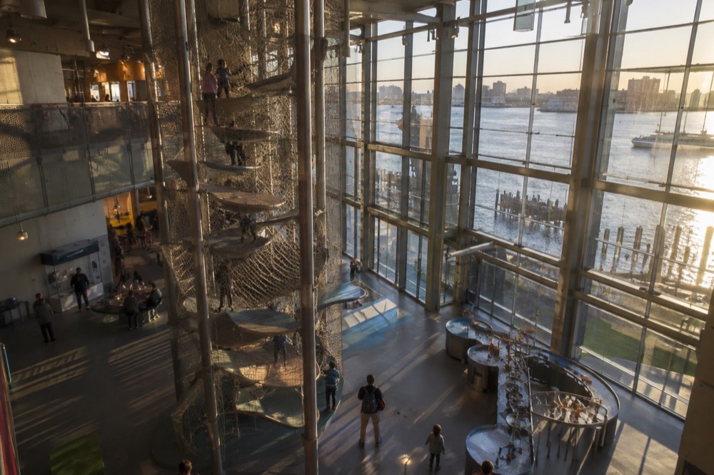 A wide view of a museum atrium with a tall climbing structure and children on its platforms