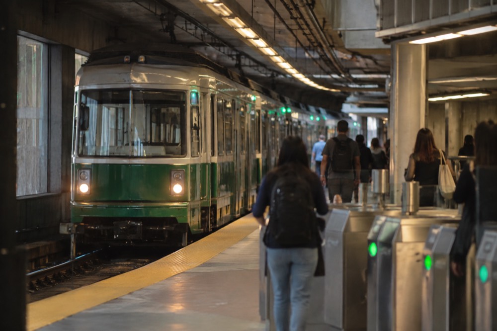 Green line trolley arriving at an underground station with turnstiles and passengers