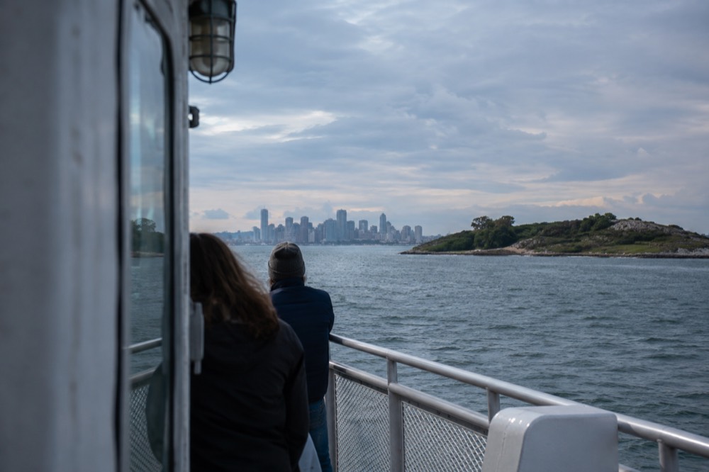 A ferry crossing open water toward green islands in Boston Harbor with the city skyline behind