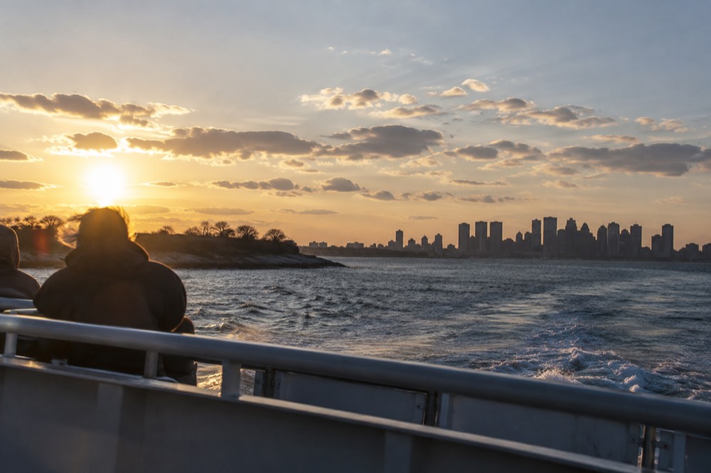 A ferry pulling away from an island dock toward the Boston skyline at golden hour
