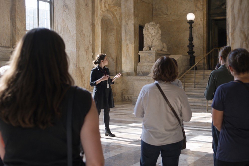Docent speaking to a small group of visitors in a marble gallery with murals