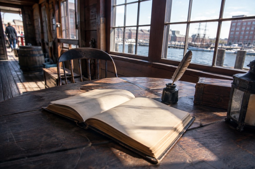 Open book and quill on a wooden table in an eighteenth-century styled room