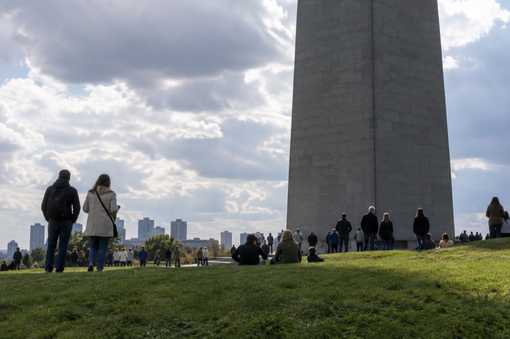 Visitors gathered on a grassy slope around the base of a granite monument