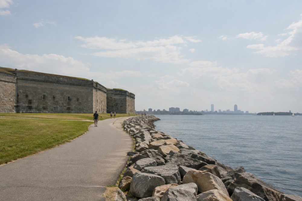 A granite fortification beside a harbor shoreline with a walking path and open water beyond