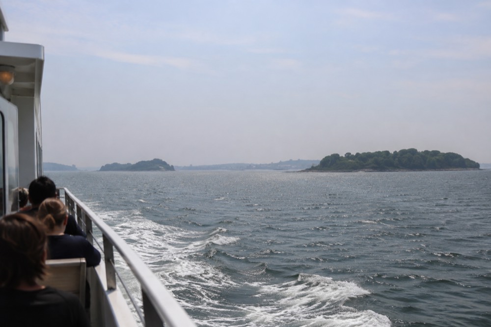 A ferry boat crossing open harbor water toward green islands on the horizon