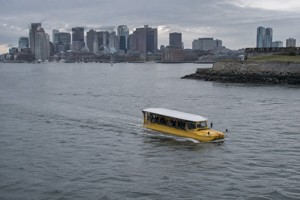 An amphibious tour boat motoring on a river with a city skyline behind it