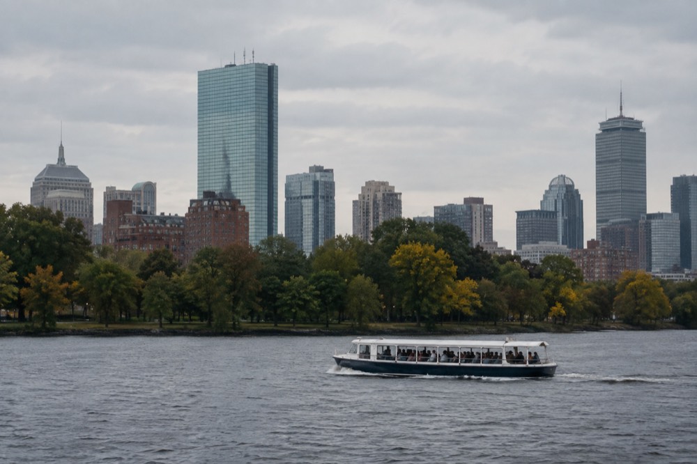 A sightseeing boat cruising on the Charles River basin with the Boston skyline above the trees