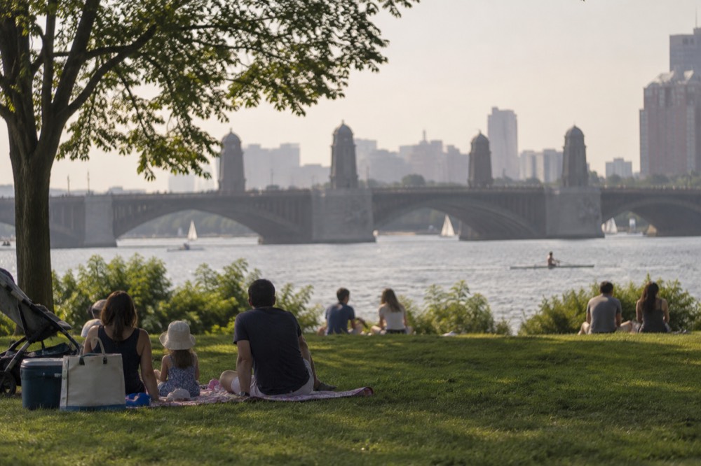Families picnicking on a grassy riverside lawn with the Longfellow Bridge in the distance