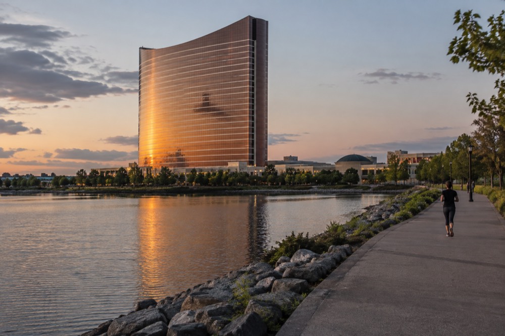 The curved glass hotel tower of Encore Boston Harbor reflected in the Mystic River at dusk