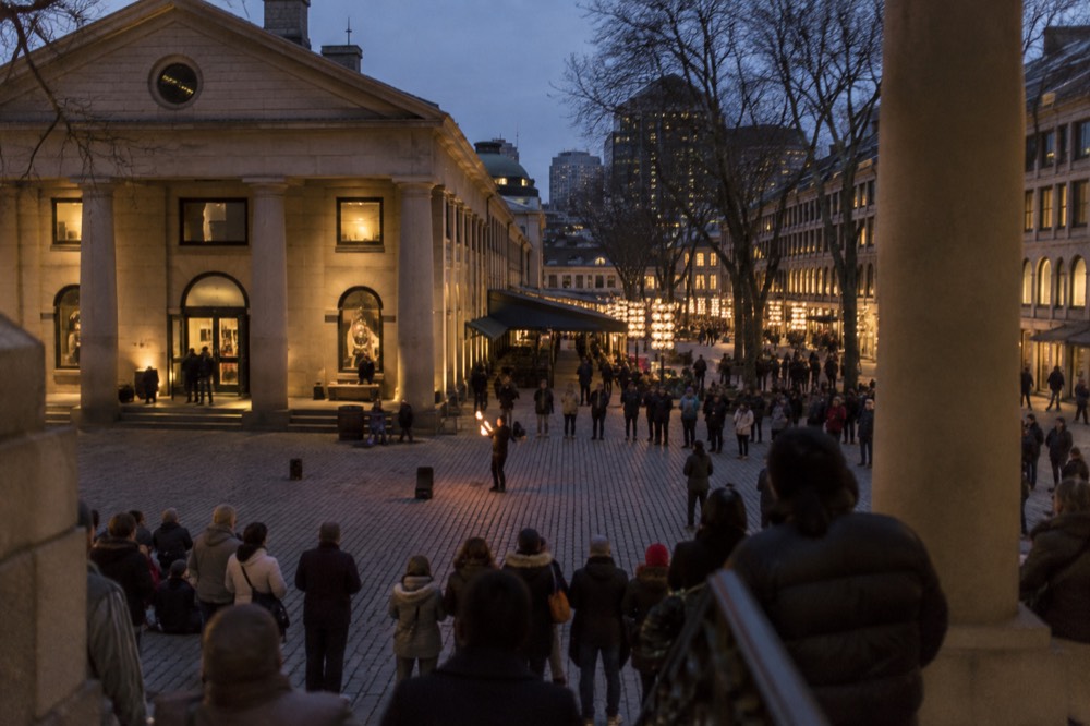 Cobblestone plaza between Faneuil Hall and the market buildings with a street performer and a crowd