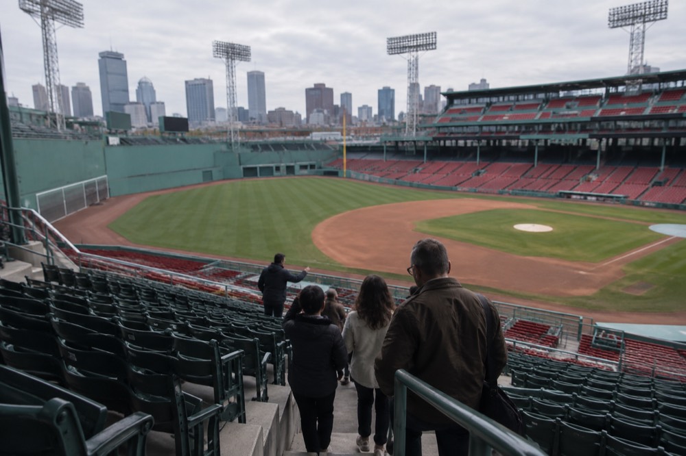 A guide in a ballpark interior leading a small group of visitors past the seating sections