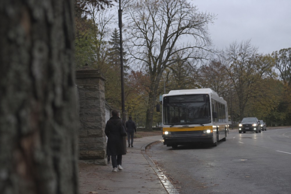 An MBTA bus approaching a stop near a leafy urban park entrance