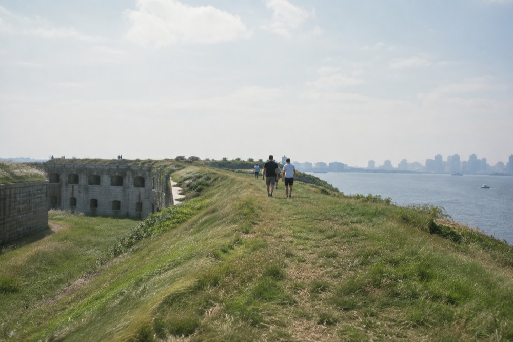 Visitors walking the grassy ramparts of Fort Warren with harbor water on both sides