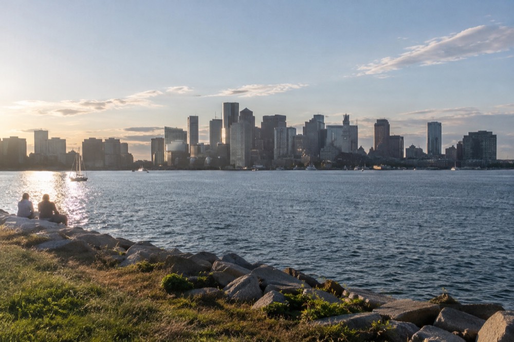The Boston skyline seen across open harbor water from an island shoreline