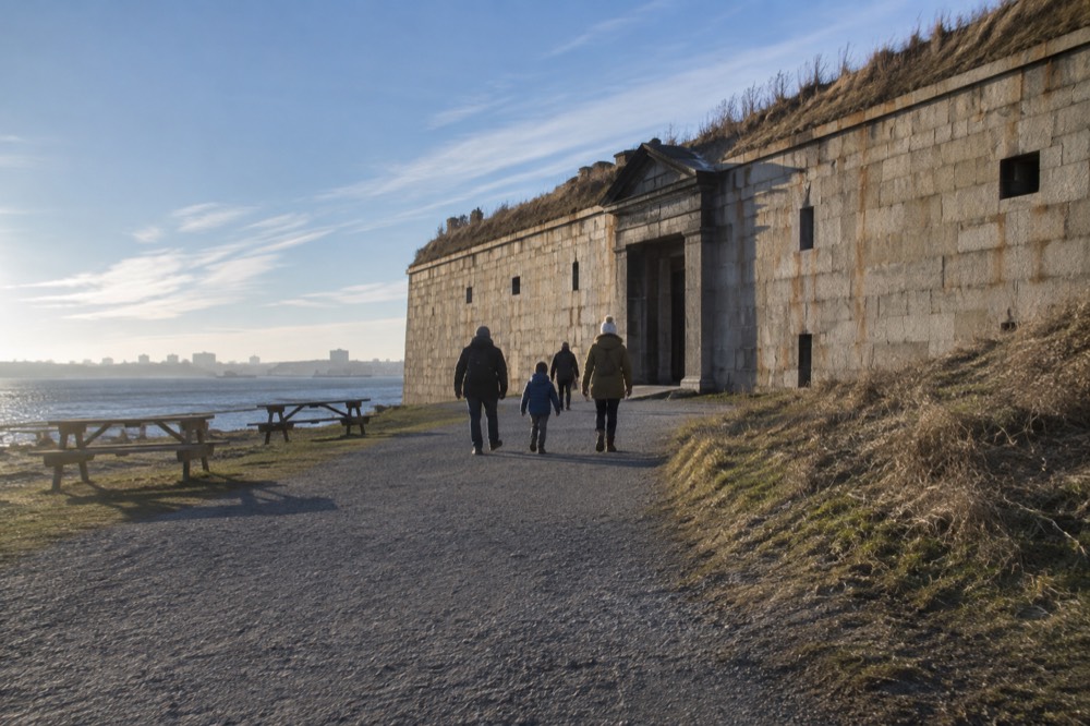 A family walking a gravel path toward the fort entrance with picnic tables nearby