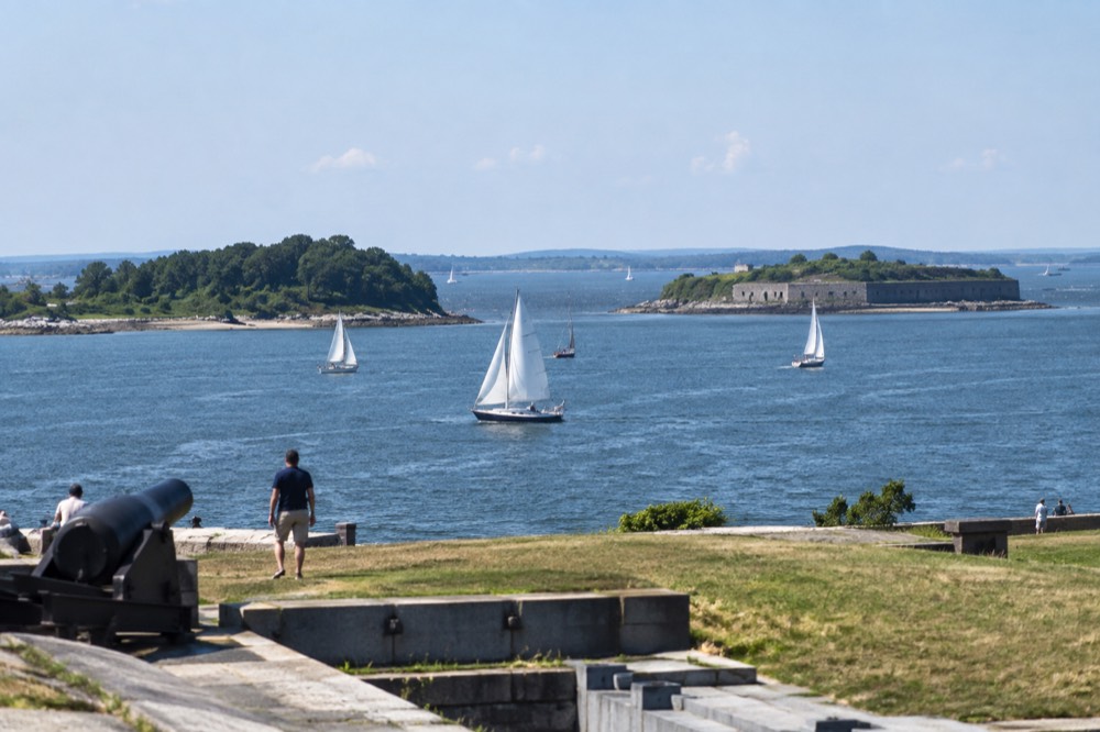 Two islands seen across harbor water with sailboats in the channel between them