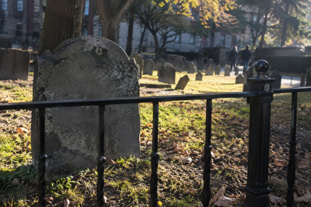 A weathered slate slab behind a low iron railing in a colonial Boston burying ground