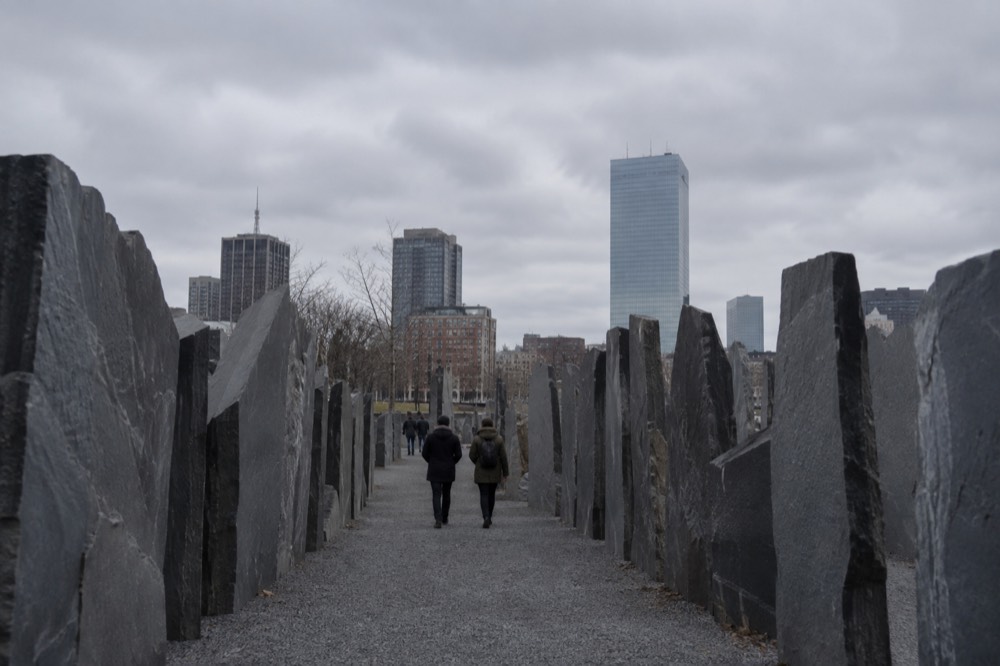 Visitors walking a gravel path between dense rows of slate slabs in downtown Boston