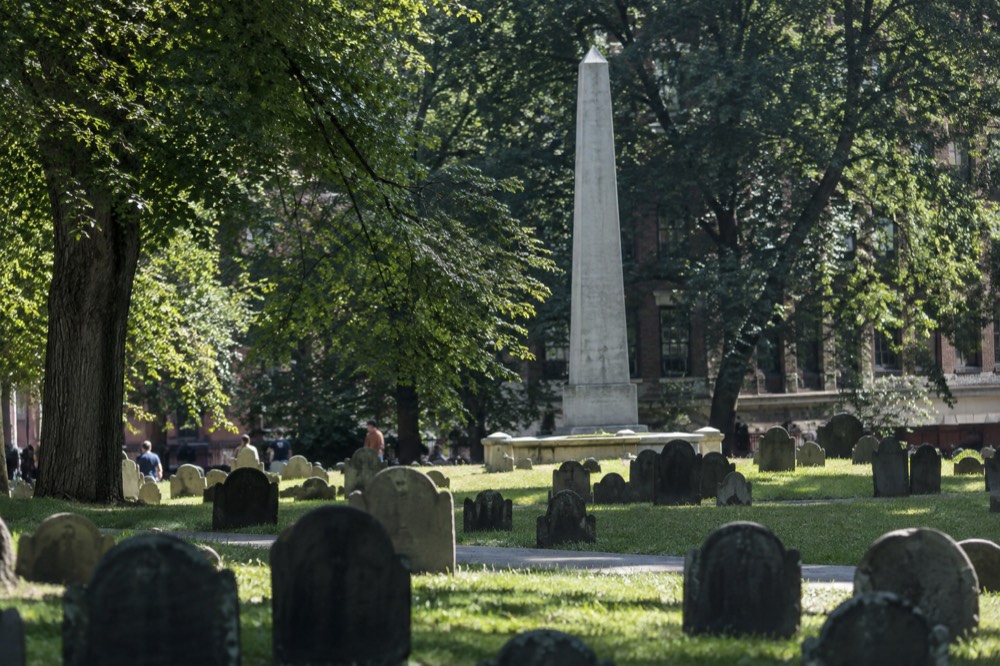 A tall granite obelisk above rows of small slate slabs under green grass