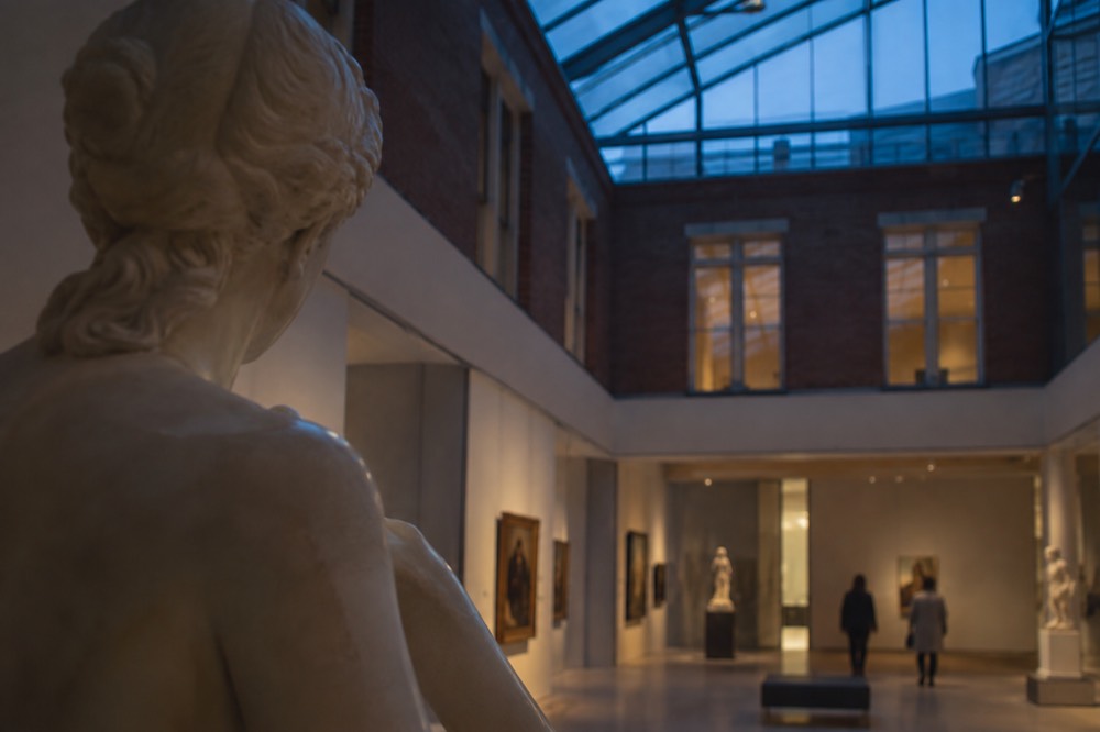 A gallery hall with sculptures and paintings under natural light