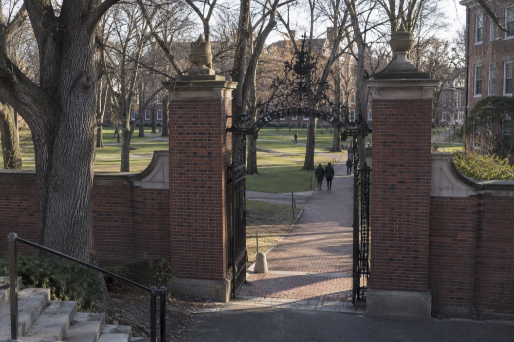 Red brick Harvard Yard gate with green lawn and mature trees beyond it