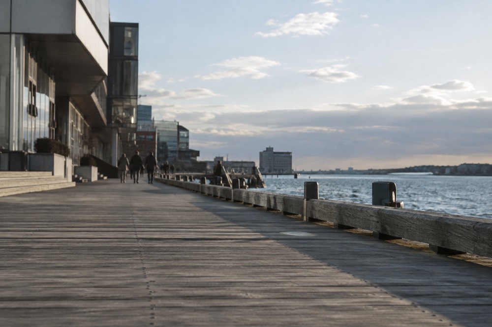 A wide boardwalk along Boston Harbor with modern buildings on one side