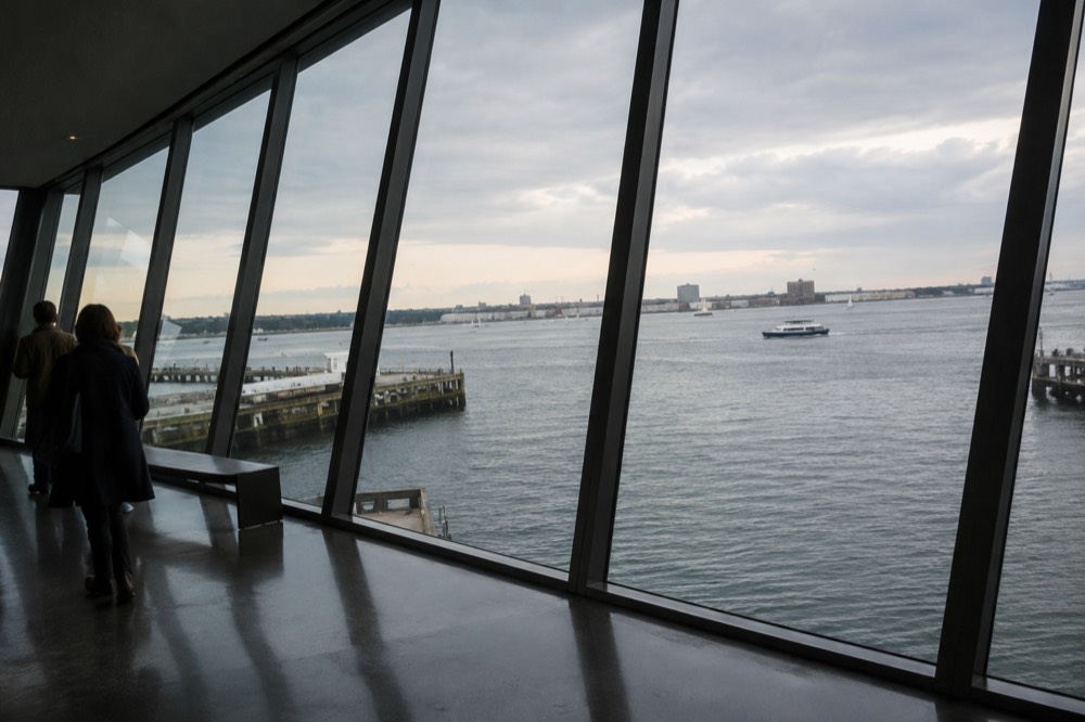 A tilted glass wall in a museum room looking down toward harbor water
