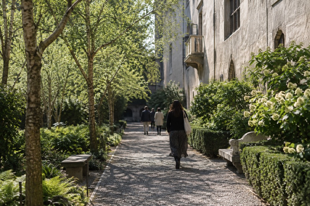 People walking along a tree-lined path beside a museum building on a mild day