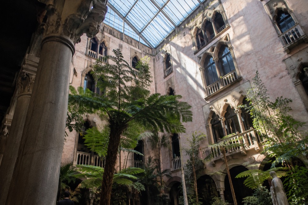 A museum courtyard with stone arches, columns and plants under a bright glass ceiling