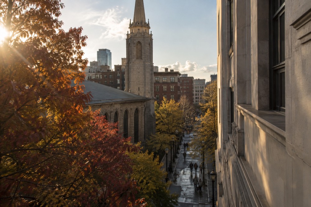 Stone church tower rising above a narrow Boston street with autumn trees