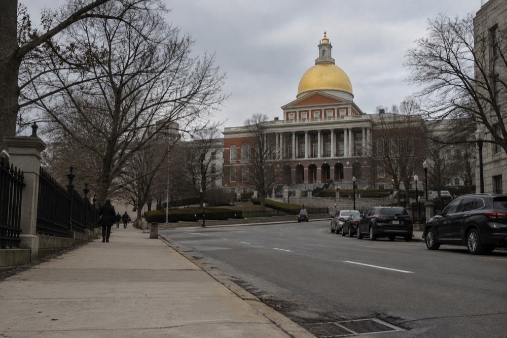 A golden domed statehouse building on a hill above a tree-lined Boston street