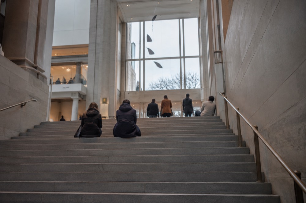 A wide staircase inside a museum with visitors resting on the steps