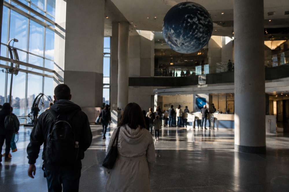 Visitors entering a museum lobby beneath a high ceiling with ticket desks ahead
