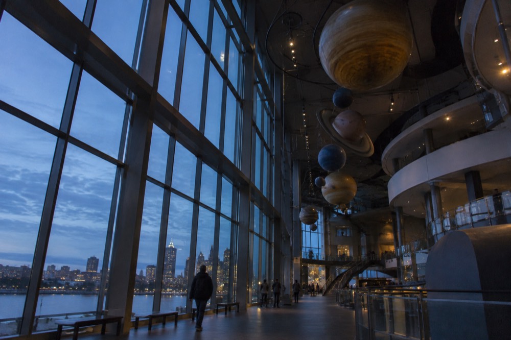 A gallery hall with large exhibit displays and a high glass ceiling above visitors