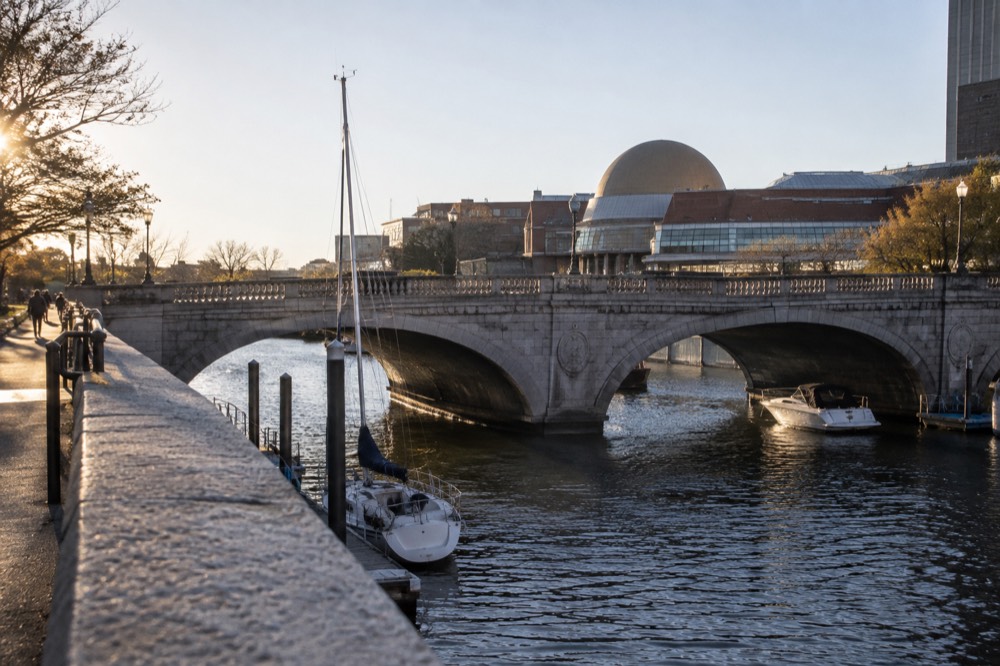 A stone bridge over river locks with a museum dome in the background and boats below