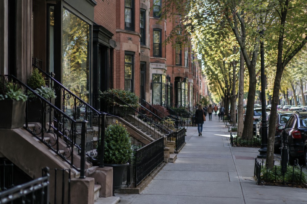 Row of brick brownstone buildings housing shops along a tree-lined Boston street
