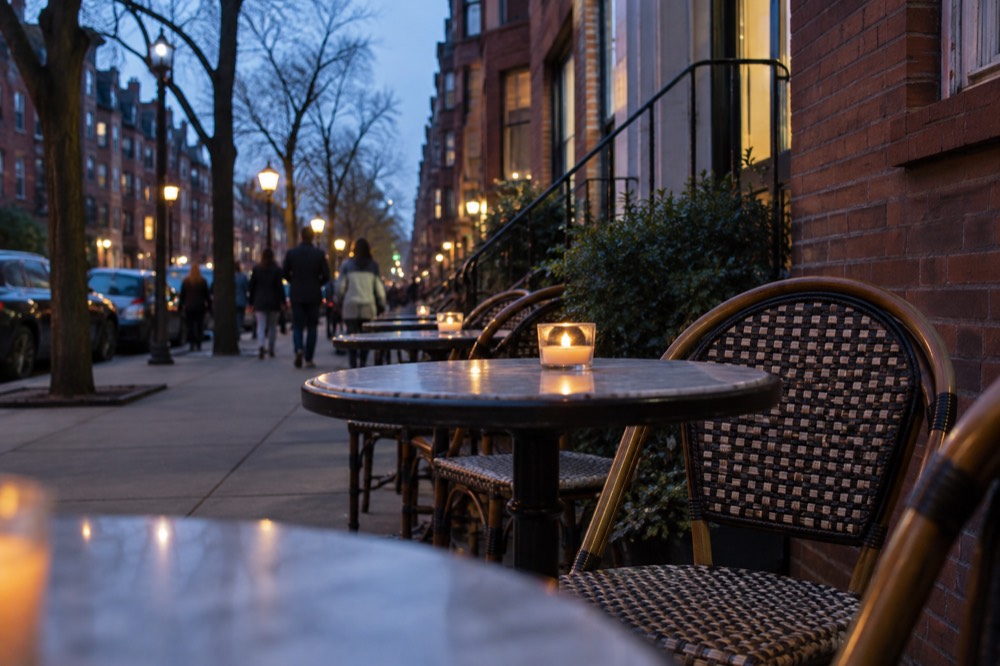 Outdoor cafe tables beside a brick building on a busy city street