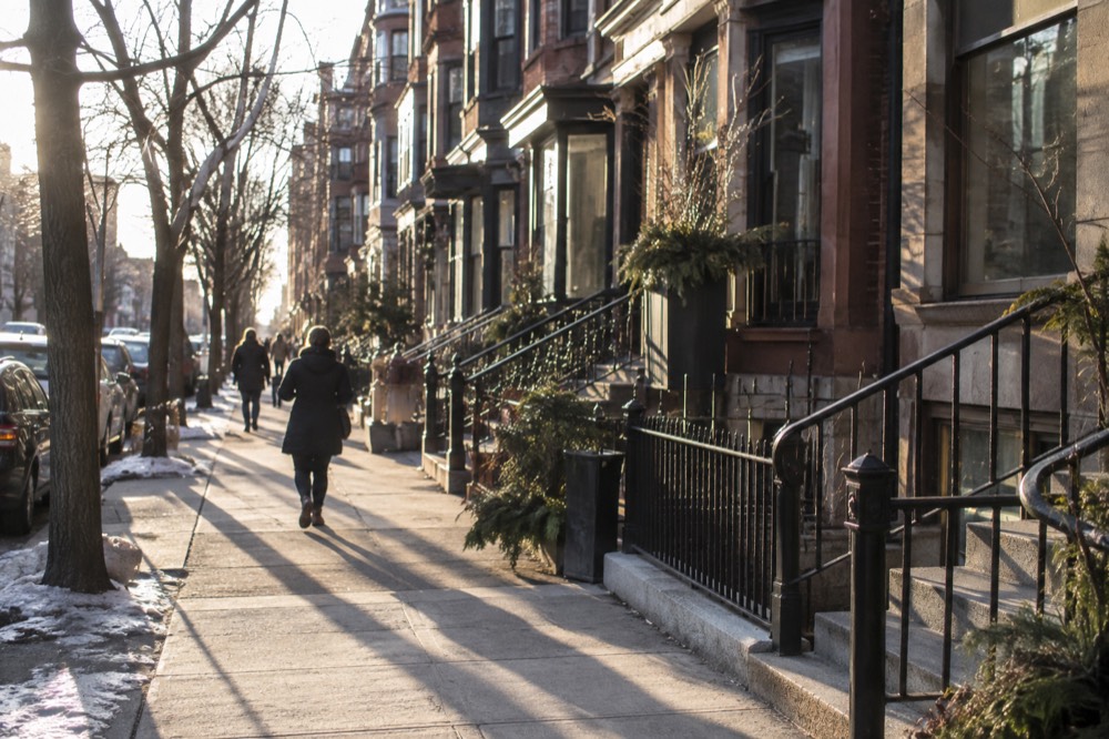 Shoppers passing a row of small storefronts in brick townhouses