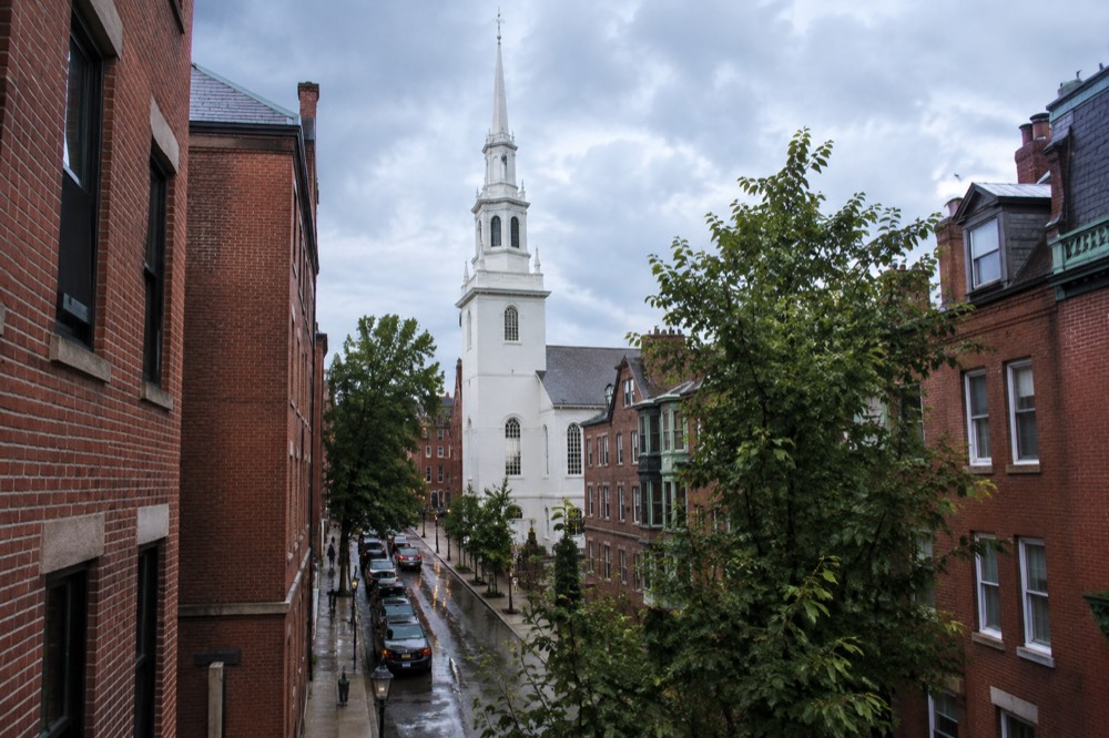 White clapboard church with a tall steeple rising above brick buildings in Boston's North End
