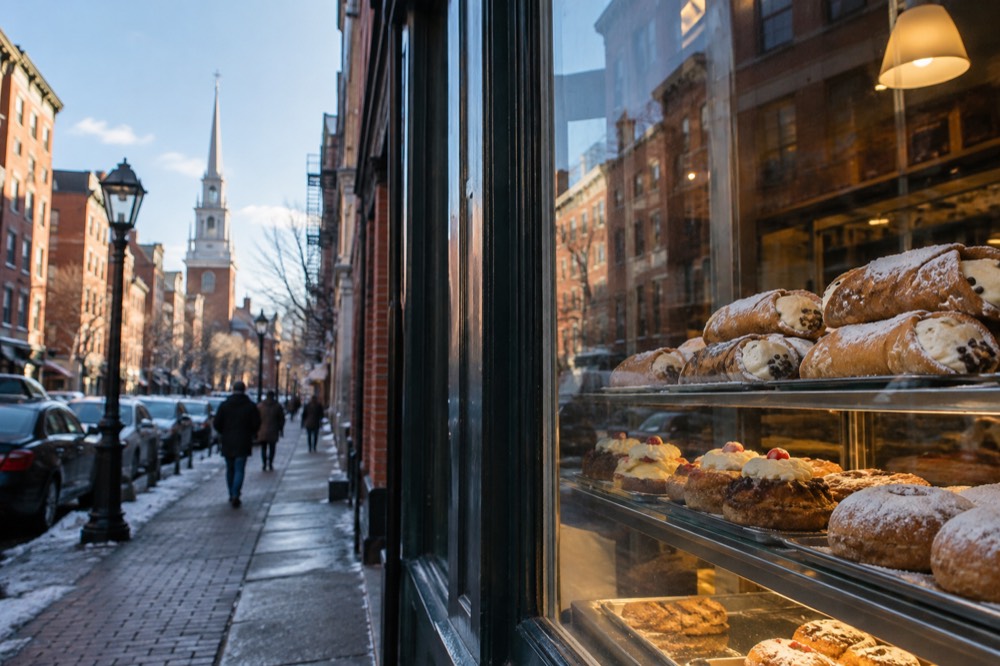 Cannoli and pastries displayed in a bakery window on a busy North End street