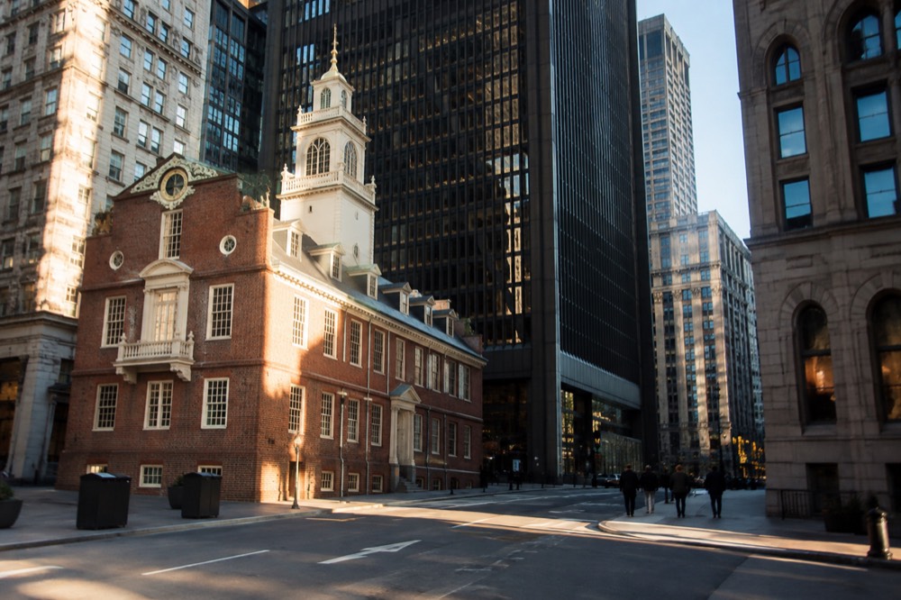 The brick Old State House with its white tower and balcony standing between modern office towers in downtown Boston