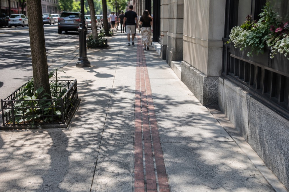 A double line of red bricks marking the Freedom Trail running along a downtown Boston sidewalk