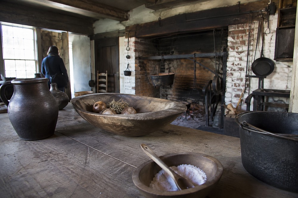 A colonial-era kitchen interior with iron cookware and a low ceiling